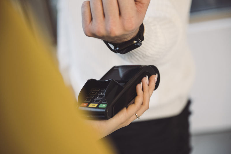 Man paying through smart watch to waitress holding credit card reader in cafe