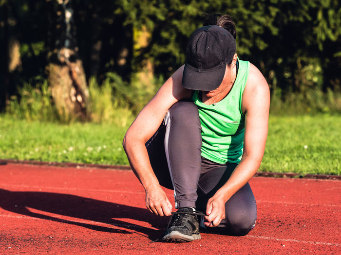 Female asian runner in green singlet stopped for lacing her sneakers. health and sport concept