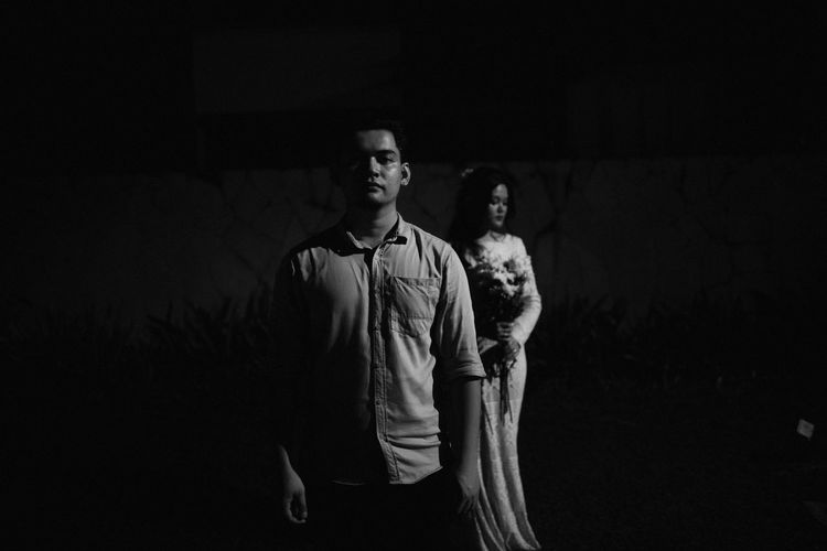Full length of man looking away while standing against wall at night