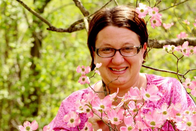Portrait of smiling woman standing by pink flowers growing outdoors