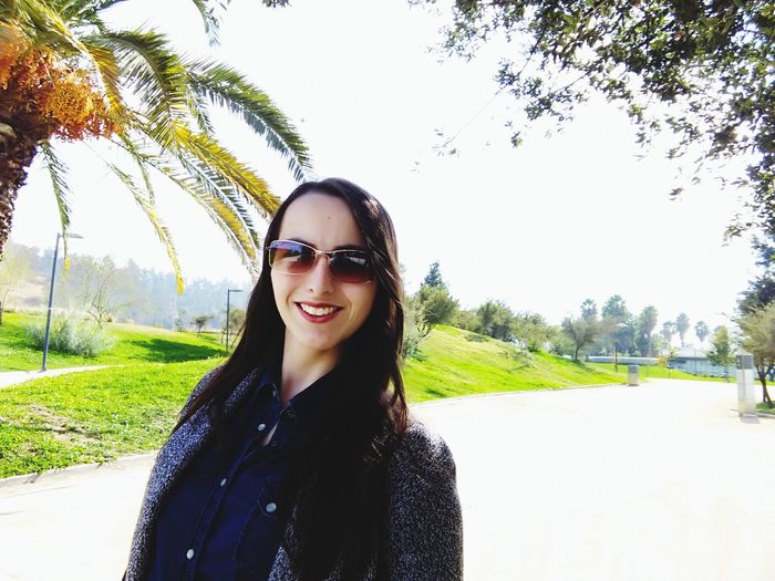 Portrait of smiling young woman wearing sunglasses against trees