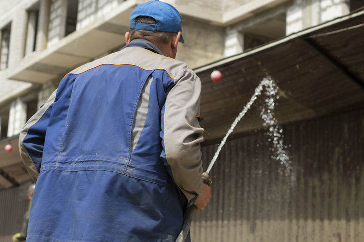 A man washes the fence with a hose. the builder cleans the fence from dirt. 