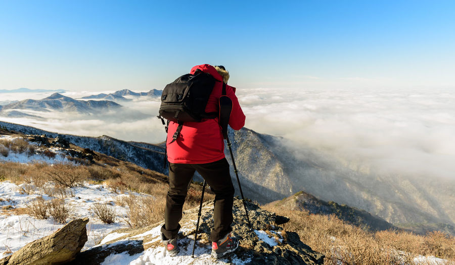 Man taking photo of snow covered mountain against sky