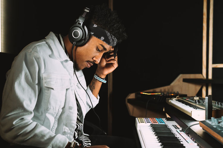 African american male musician playing electric piano while rehearsing music in recording studio