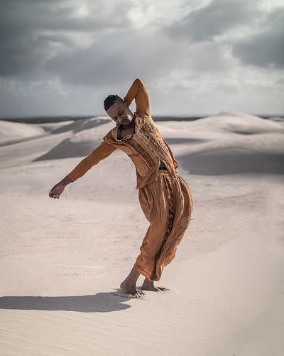 Man in traditional clothing posing on sand at beach against sky