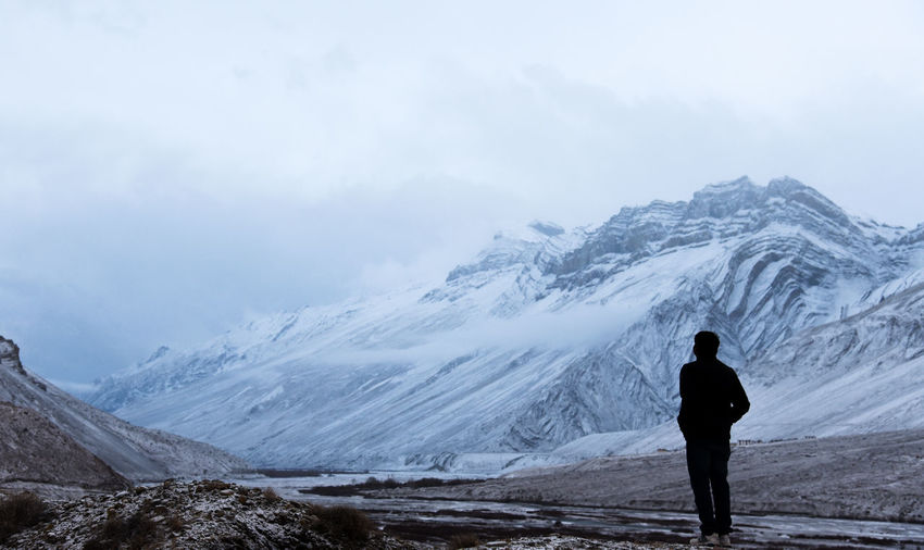 Rear view of person standing by snowcapped mountain against sky