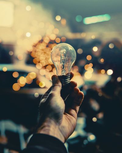 Midsection of person holding illuminated light bulb with bokeh background