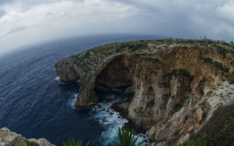 Rock formations by sea against sky at blue grotto, malta