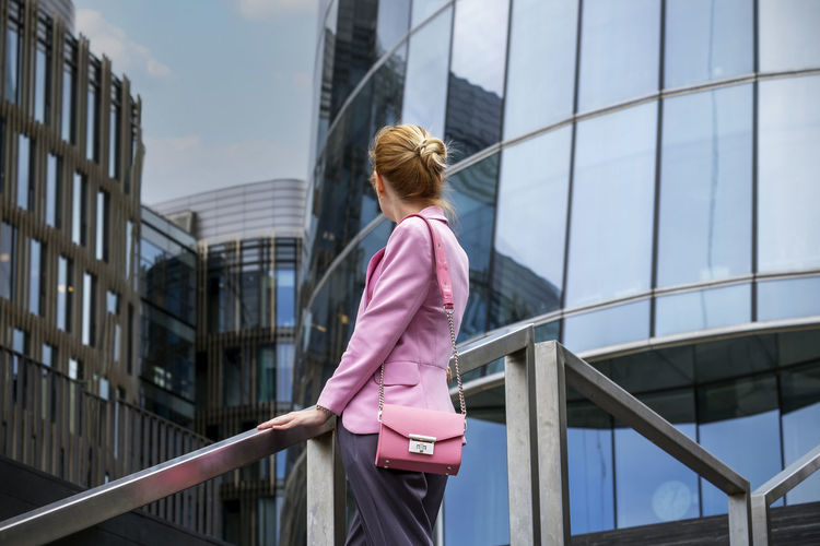 Young woman stands on steps with her back to camera and looks at modern office building