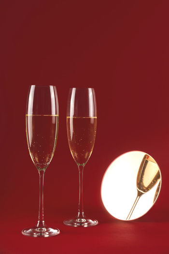 Two glassess of champagne with reflection in a small round mirror on a red background.