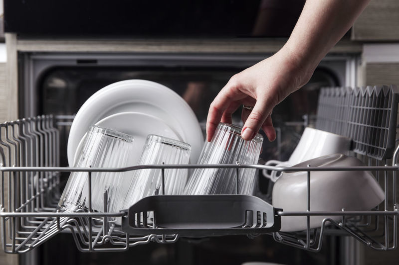 Female hand loading dished to, empty out or unloading from dishwasher machine with clean utensils