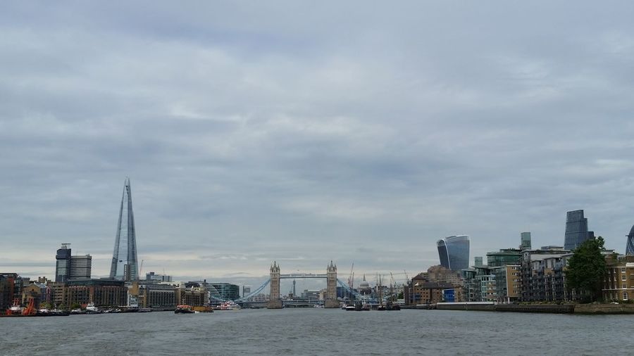 Thames river amidst buildings against cloudy sky