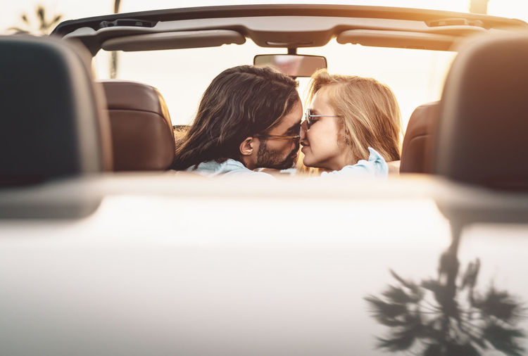 Man and woman kissing while sitting in car against sky
