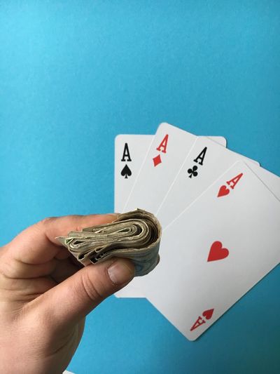 Cropped image of hand holding paper currency with aces cards at casino table