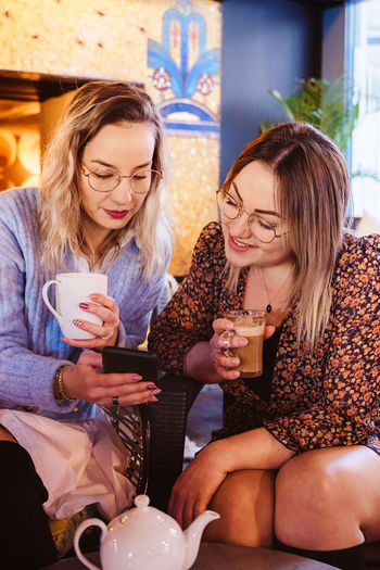 Young women using phone while holding coffee