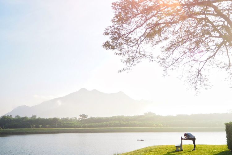 Scenic view of lake against sky with woman who  is doing yoga