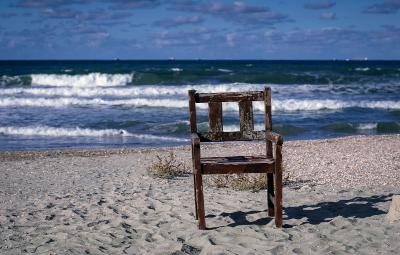 Chair on shore at beach against sky