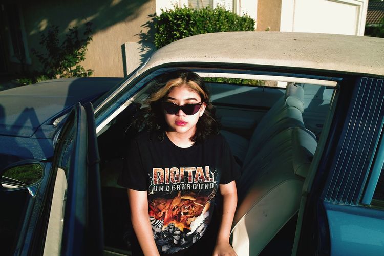 PORTRAIT OF YOUNG WOMAN WEARING SUNGLASSES SITTING ON CAR