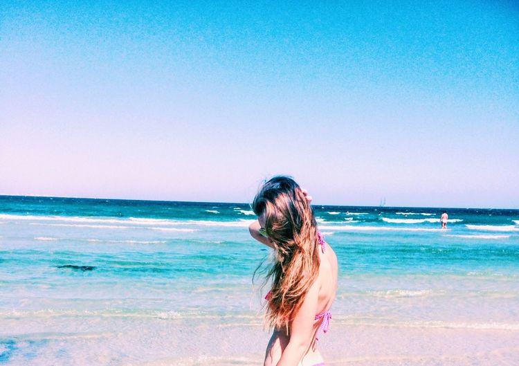 Beautiful young woman posing at beach against sky