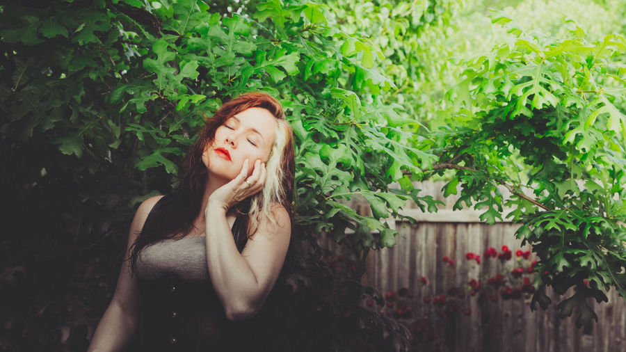 Beautiful woman touching her cheek against trees in yard