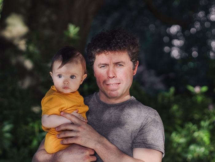 Caucasian handsome and young dad holds his little young daughter in his arms in a yellow bodysuit