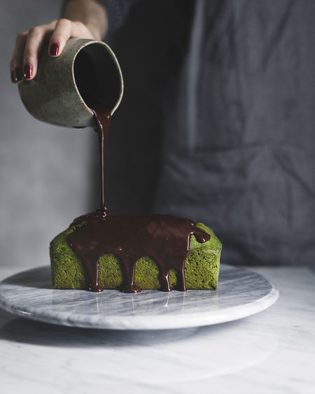 Midsection of woman pouring chocolate sauce on matcha pound cake