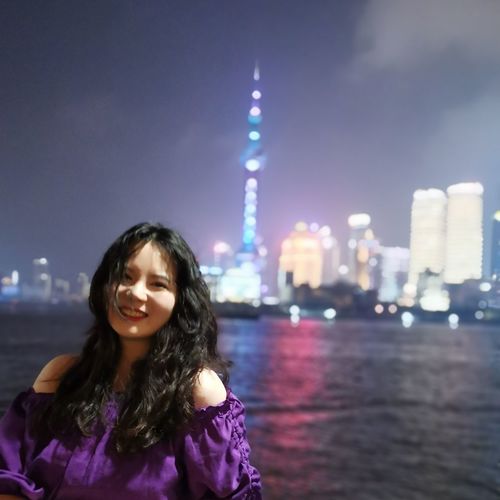 Portrait of smiling woman against illuminated city at night