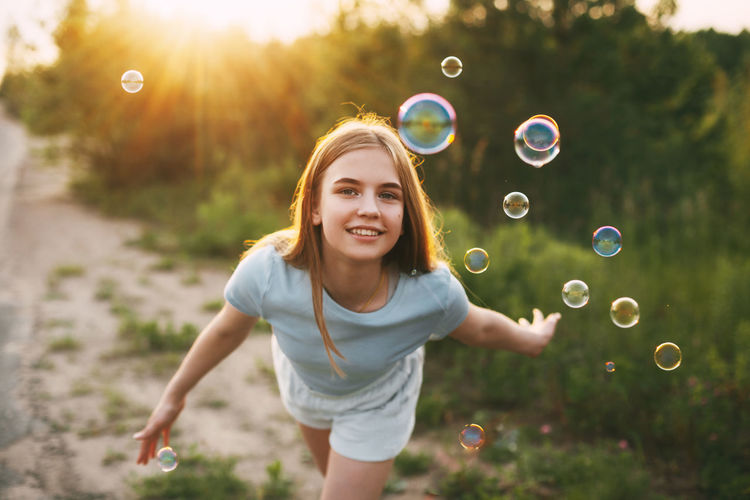 Portrait of smiling girl playing with bubbles in park at sunset