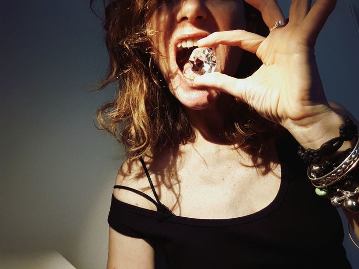 Low angle view of woman holding diamond against open mouth