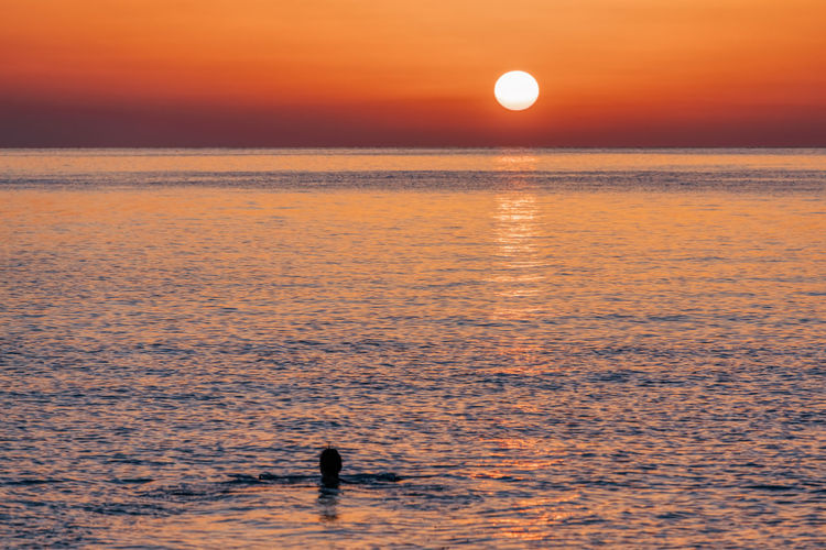 Silhouette person on sea against orange sky during sunset