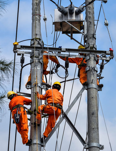 Low angle view of people working on electricity pylon against sky