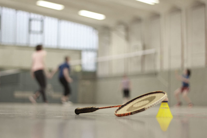 Close-up of badminton racket and shuttlecock on court against people