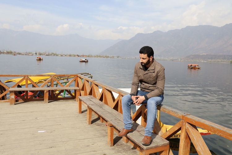 Man sitting on wooden pier at lake against sky, dal lake srinagar 