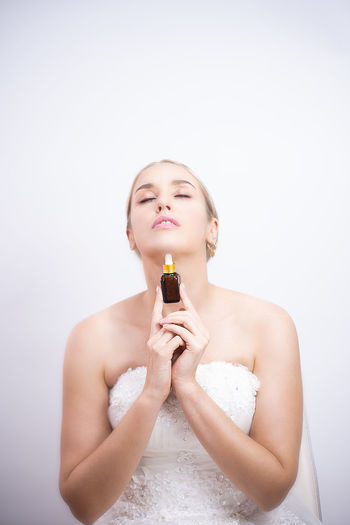 Beautiful young woman holding essential oil over white background