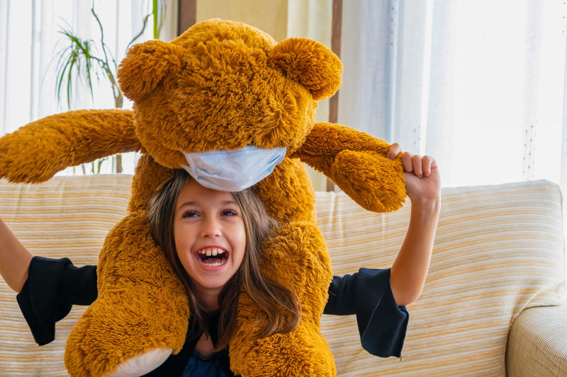 Cheerful girl carrying teddy bear on shoulders at home