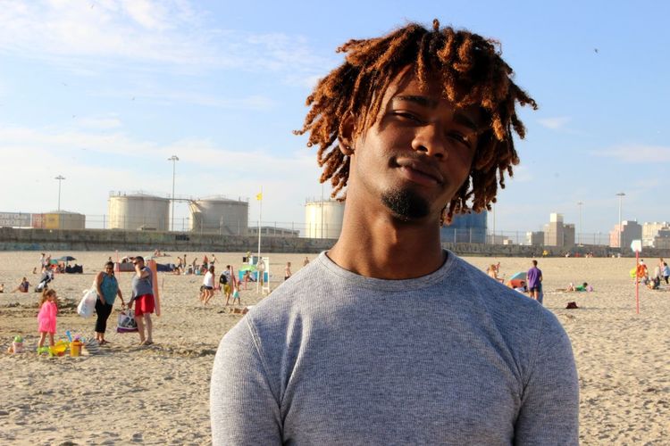 Portrait of young man with dreadlocks standing at beach against sky