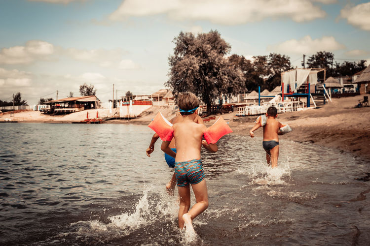 Rear view of boys having fun while running through sea in summer day.