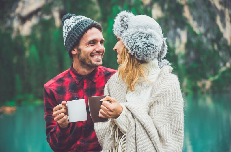 Close-up of couple holding coffee cup standing against lake