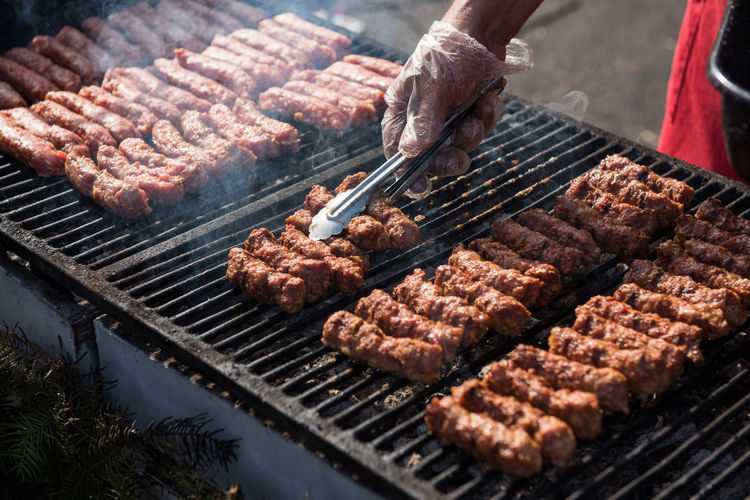 Cropped hand of man preparing meat on barbecue grill