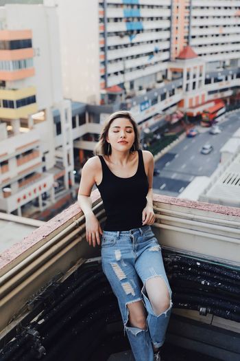 High angle view of young woman wearing torn jeans standing against building in balcony