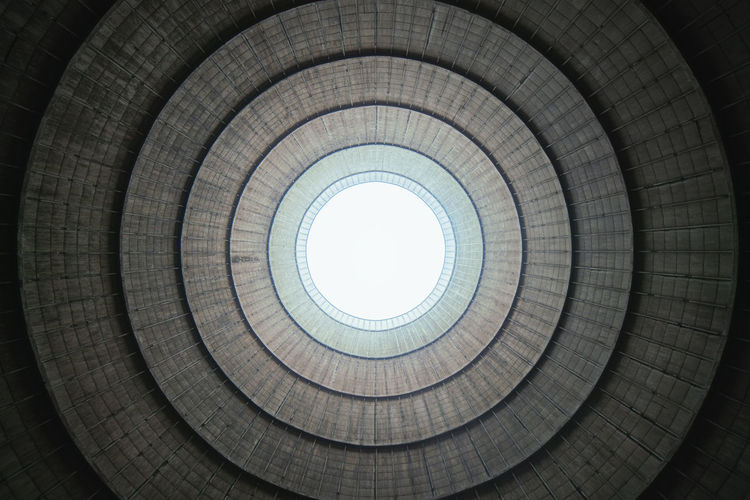 From below sunlight shining through round hole in ceiling of industrial facility in daytime