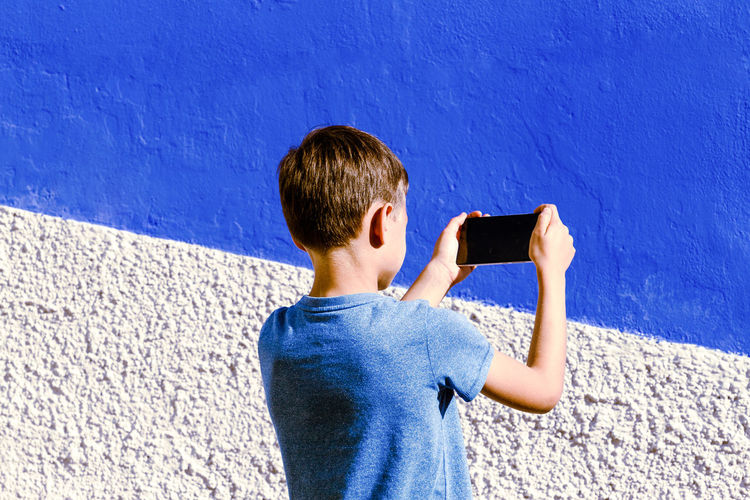 Boy photographing against blue wall