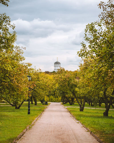 Footpath amidst trees in park against sky during autumn