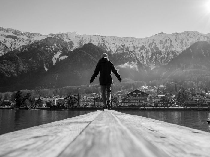 Rear view of person walking on pier over lake against mountains