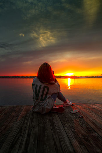 Rear view of woman sitting on pier in lake against sky