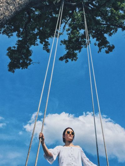 Low angle view of woman holding ropes while standing against sky