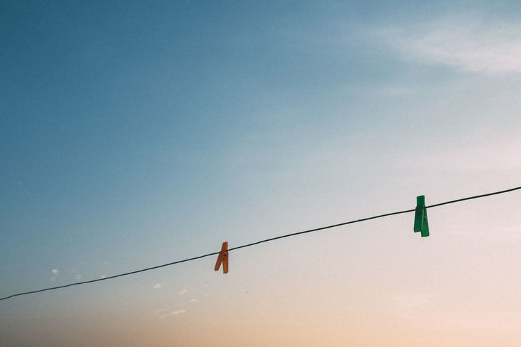Low angle view of clothespin hanging on rope against sky during sunset