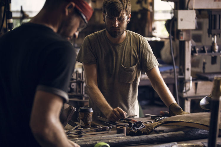 Blacksmith looking at coworker working at table in workshop