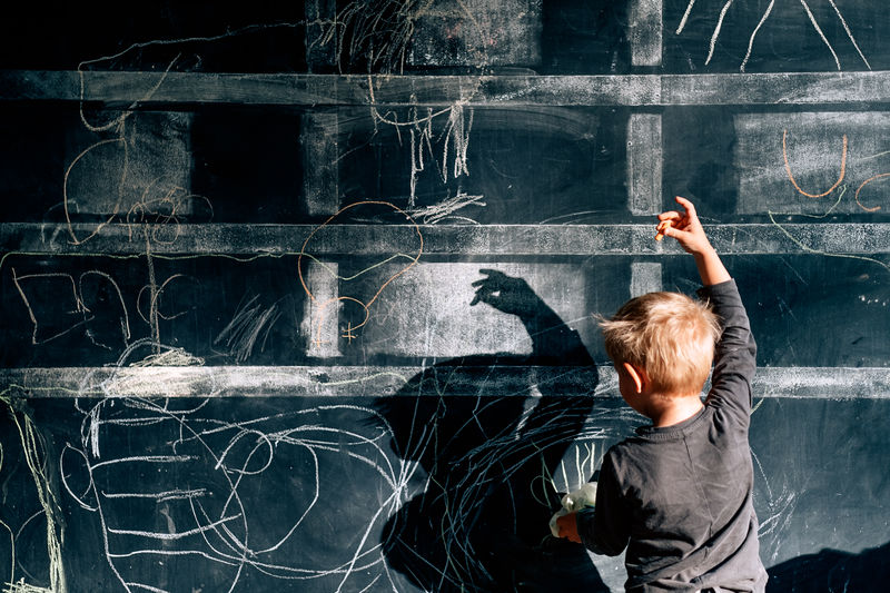Rear view of boy dancing while looking at shadow on blackboard
