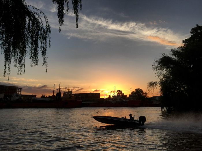 Silhouette boat in river against sky during sunset